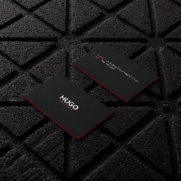 Dwie czarne wizytówki z czerwonymi krawędziami leżące na czarnym, teksturowanym tle. Na jednej widoczne logo 'HUGO SOLUTIONS' w kolorze białym, na drugiej dane kontaktowe.