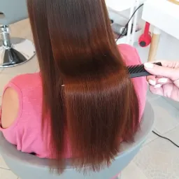 Proste, lśniące, brązowe włosy klientki podczas czesania grzebieniem w salonie, widok z tyłu.