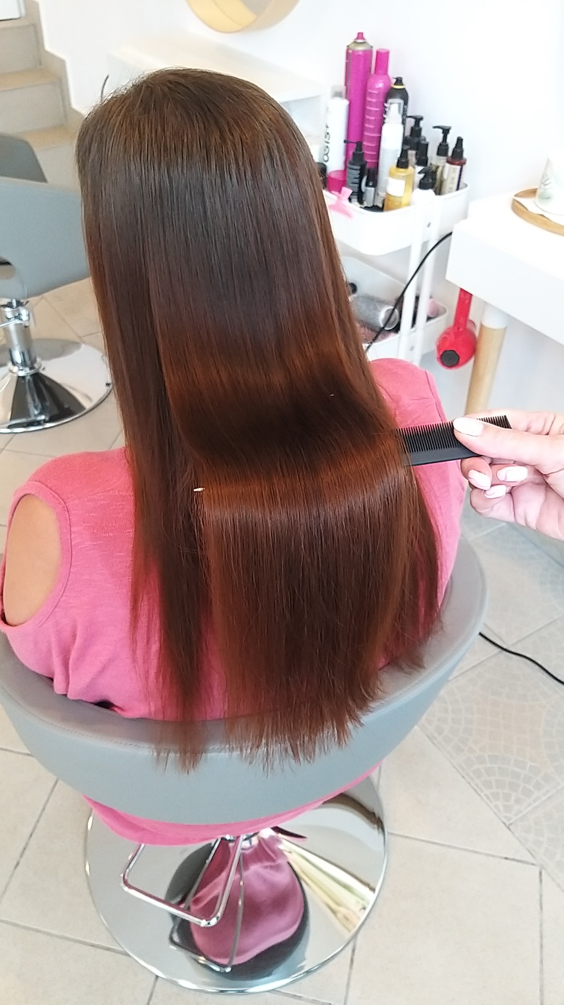 Proste, lśniące, brązowe włosy klientki podczas czesania grzebieniem w salonie, widok z tyłu.
