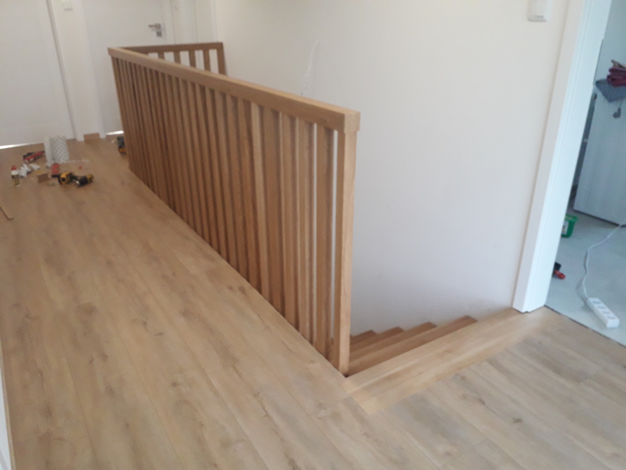 Montaż podłogi drewnianej i balustrady schodowej z jasnego drewna, widoczne narzędzia i materiały budowlane na podłodze.
