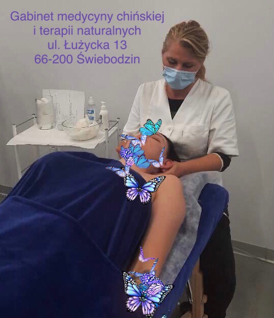 Kobieta w masce wykonuje zabieg na pacjentce leżącej na niebieskim łóżku; twarz pacjentki zasłonięta grafiką motyli; w tle gabinet medycyny chińskiej i terapii naturalnych.