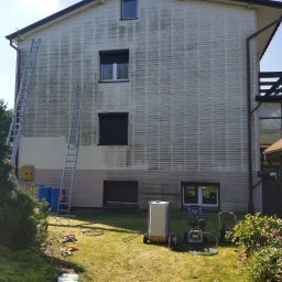 ECO-TECH Przemysław Szubert - Boczna ściana domu z sidingiem, częściowo oczyszczona z zabrudzeń, dwie drabiny opierają się o ścianę, na trawniku rozłożone narzędzia i sprzęt do czyszczenia.