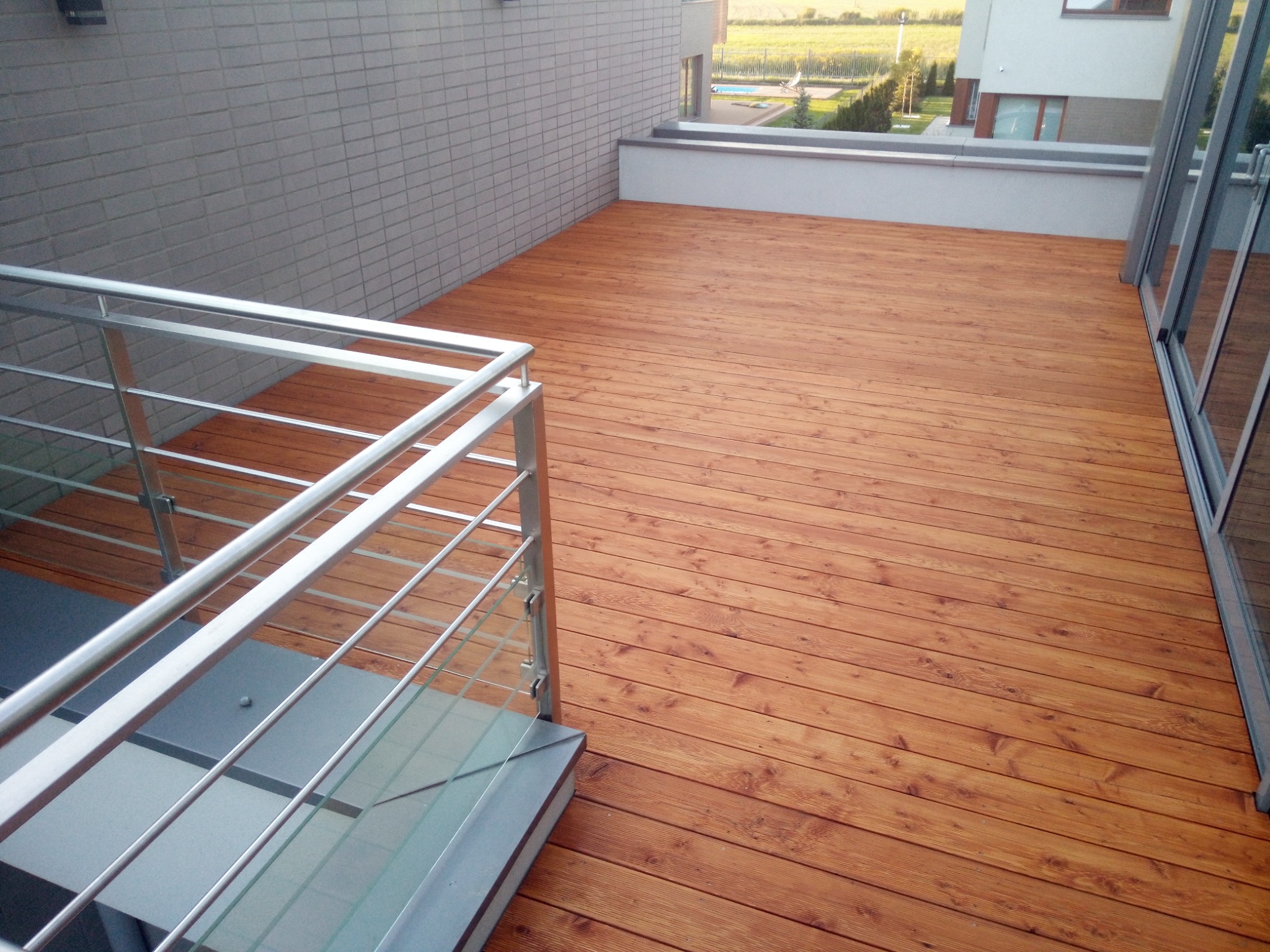 Nowoczesny taras na dachu budynku z drewnianą podłogą, szklaną balustradą i widokiem na okolicę.