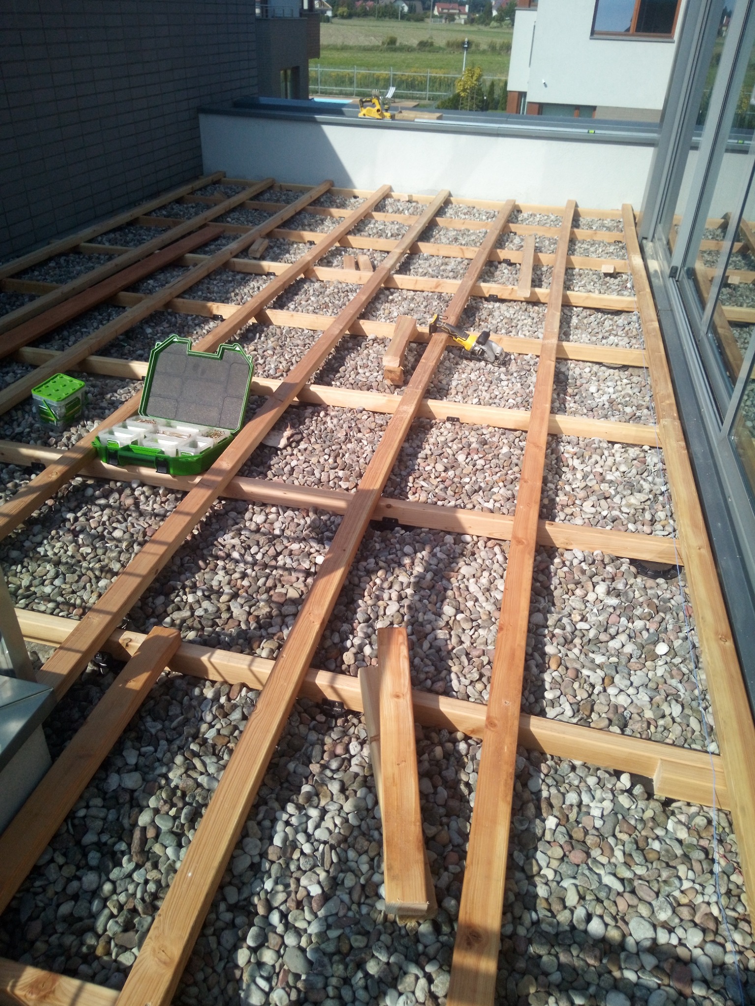 Konstrukcja drewniana pod taras na żwirowym podłożu, widoczna skrzynka z narzędziami i wkrętarka akumulatorowa.