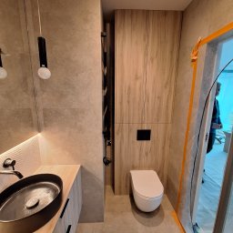 Usługi Budowlane MatBud Mateusz Malec - Nowoczesna łazienka z umywalką nablatową, podwieszaną toaletą i grzejnikiem drabinkowym. Ściany wyłożone płytkami imitującymi kamień, oświetlenie punktowe.