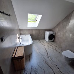 Usługi Budowlane MatBud Mateusz Malec - Wykończona łazienka na poddaszu z marmurową podłogą, białą wanną, pralką i oknem dachowym. Szaro-beżowe płytki na ścianach. Nowoczesny design.