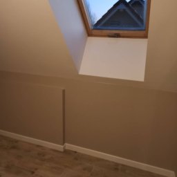 Usługi Budowlane MatBud Mateusz Malec - Poddasze po remoncie: beżowe ściany, drewnopodobne płytki na podłodze, okno dachowe z widokiem na sąsiedni dach.