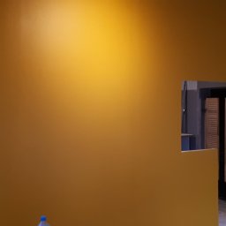 Usługi Elewacyjne Budowlane - Ściana pomalowana na kolor musztardowy, widoczny otwór drzwiowy z fragmentem łazienki w trakcie remontu, widoczne narzędzia i materiały budowlane.