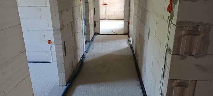 Korytarz w surowym stanie z widocznymi przewodami elektrycznymi poprowadzonymi wzdłuż ścian, puszki elektryczne w ścianach z betonu komórkowego.