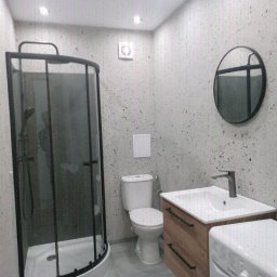 J.S.Project - Nowoczesna łazienka z kabiną prysznicową, okrągłym lustrem i pralką, wykończona w szaro-białej kolorystyce z akcentami drewna. Minimalistyczny design.