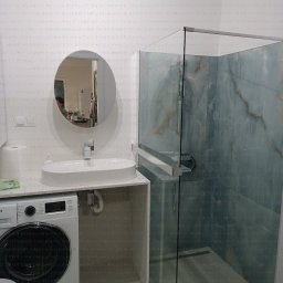 J.S.Project - Nowoczesna łazienka z kabiną prysznicową typu walk-in, owalną umywalką nablatową i pralką w zabudowie. Minimalistyczny design, jasne barwy i marmurowe wykończenie ścian.