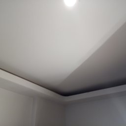 J.S.Project - Pomieszczenie po remoncie: gładkie, pomalowane na biało ściany i sufit z dekoracyjnym podwieszanym elementem przy suficie, widoczne oświetlenie.