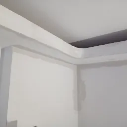Narożnik pokoju z zamontowaną płytą kartonowo-gipsową i listwą ozdobną pod sufitem, ślady szpachlowania widoczne na ścianach.
