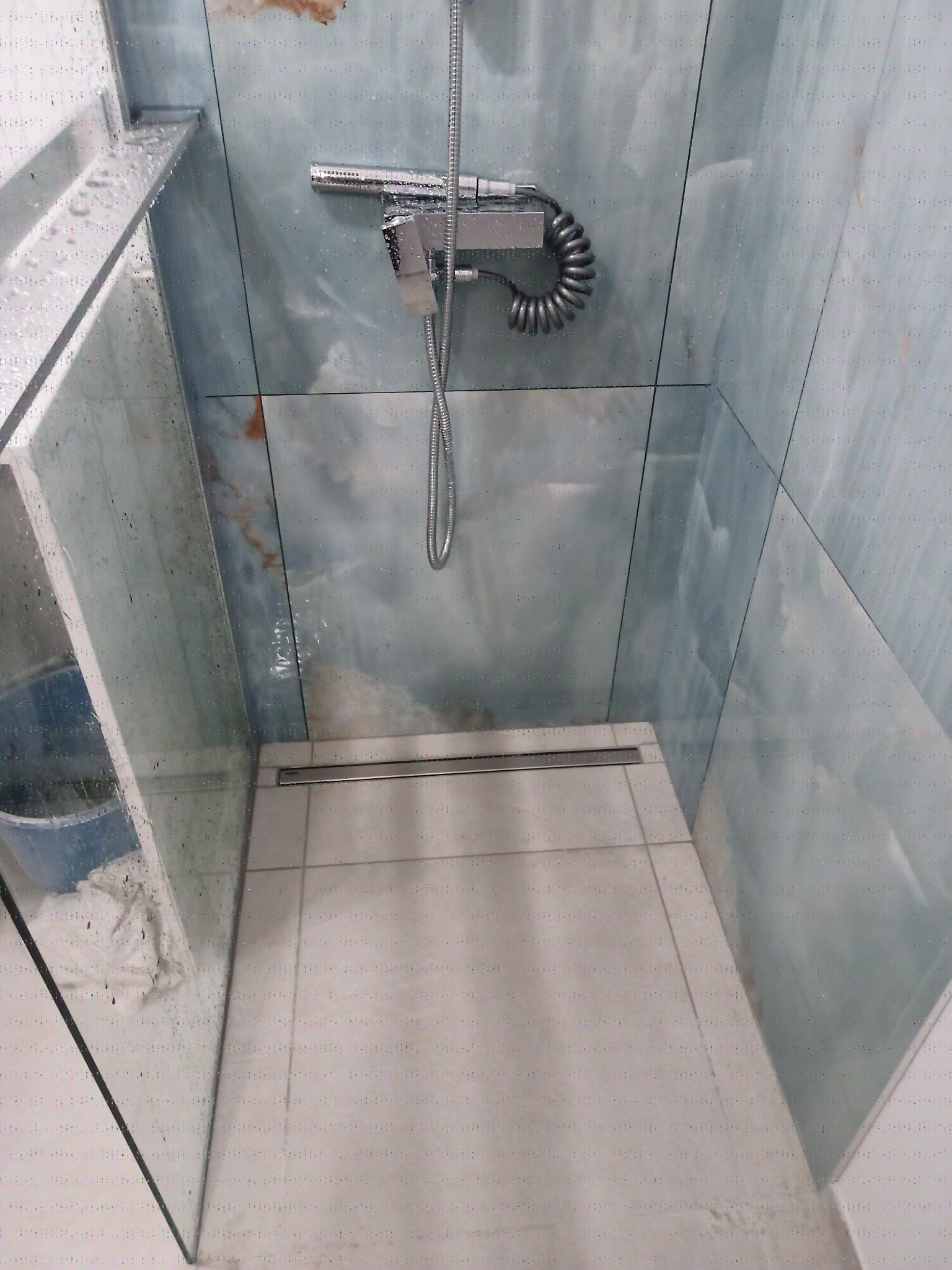 Nowoczesna kabina prysznicowa z chromowaną armaturą, wykończona płytkami imitującymi onyks, z odpływem liniowym i szklanymi ściankami, widok z góry.