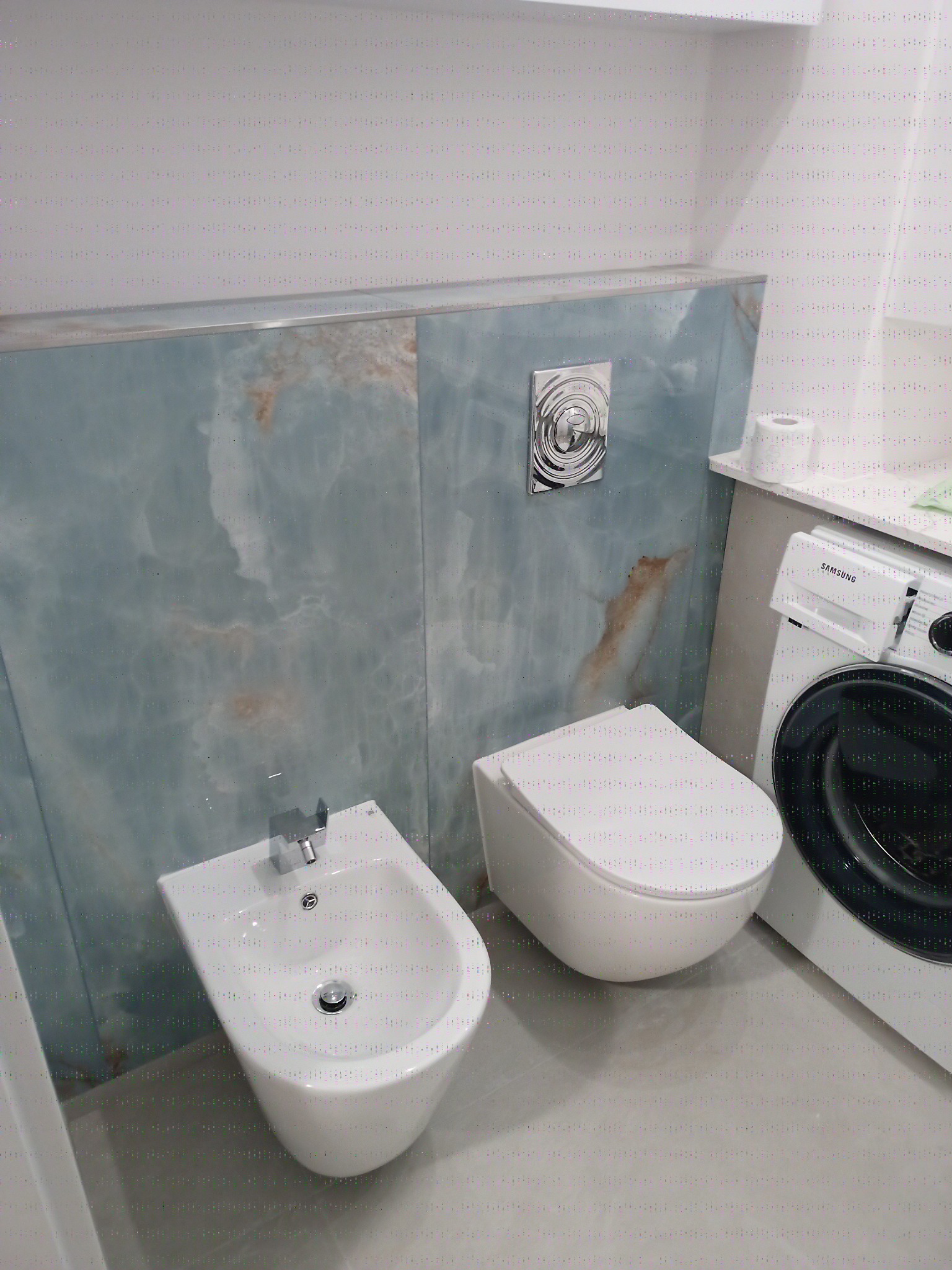 Nowoczesna łazienka z bidetem, toaletą i pralką Samsung, wykończona płytami imitującymi marmur w odcieniach błękitu i beżu. Minimalistyczny design.