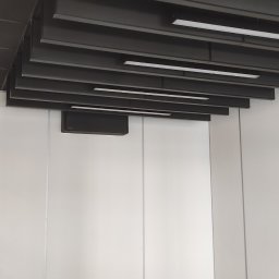 Grzegorz Smoleński - Sufit podwieszany z czarnymi panelami i oświetleniem LED w nowoczesnym biurze z białymi ścianami modułowymi i szarą podłogą.