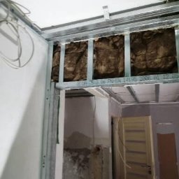Dar-Bud Usługi Remontowo Budowlane - Ocieplenie poddasza wełną mineralną w metalowej konstrukcji szkieletowej, widoczne kable i fragmenty ściany w trakcie remontu.