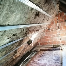 Dar-Bud Usługi Remontowo Budowlane - Poddasze w trakcie izolacji: wełna mineralna między krokwiami i profile metalowe, widoczna ściana z czerwonej cegły