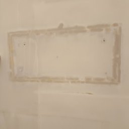 Łukasz Perliceusz - Ściana po nałożeniu gładzi szpachlowej, widoczne ślady po łataniu otworu. Powierzchnia przygotowana do dalszych prac wykończeniowych. Delikatne pęknięcie w dolnej części ściany.