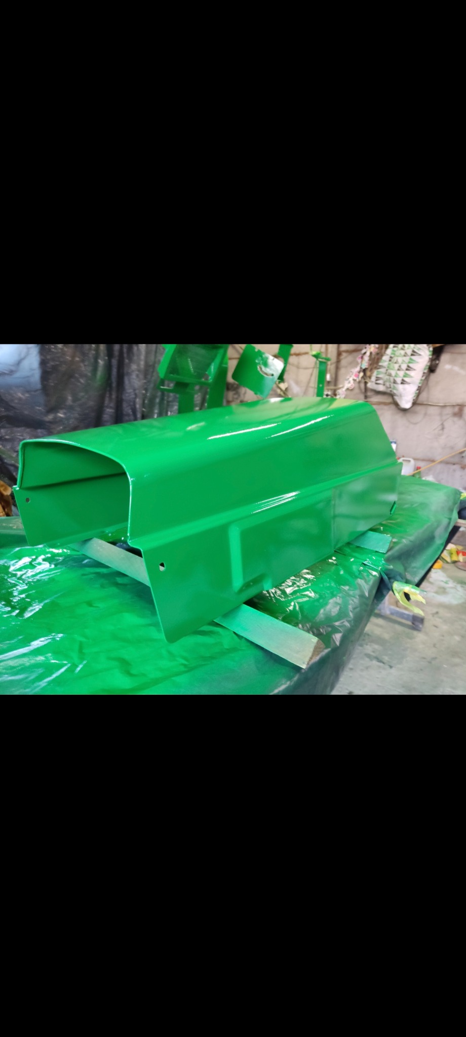 Element maszyny rolniczej po malowaniu na jaskrawy zielony kolor, leżący na folii ochronnej. Widoczne refleksy światła na świeżej powłoce lakierniczej.