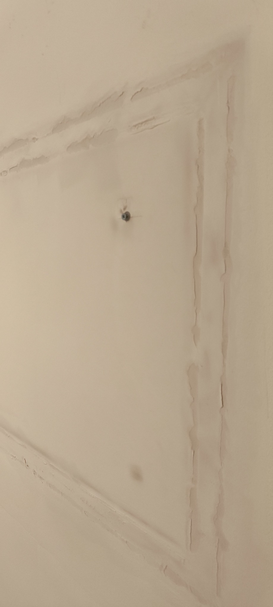 Niedokładnie pomalowany sufit z widocznymi smugami i zaciekami farby, szczególnie wzdłuż krawędzi i w okolicy otworu po lampie. Widoczne niedociągnięcia i nierówności.