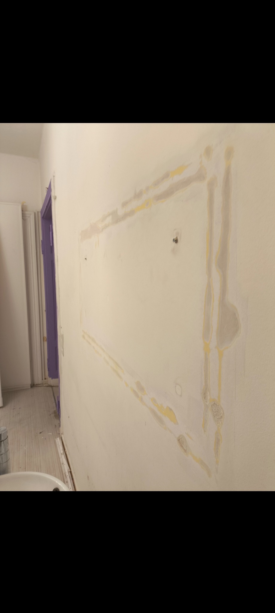 Ściana w trakcie prac wykończeniowych: widoczne ślady po szpachlowaniu wokół miejsca po usuniętej ramie, przygotowanie do dalszych prac malarskich w pomieszczeniu.