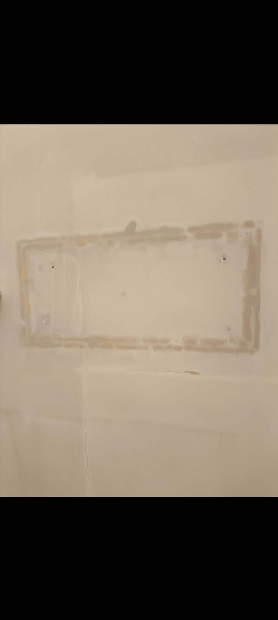 Ściana po nałożeniu gładzi szpachlowej, widoczne ślady po łataniu otworu. Powierzchnia przygotowana do dalszych prac wykończeniowych. Delikatne pęknięcie w dolnej części ściany.