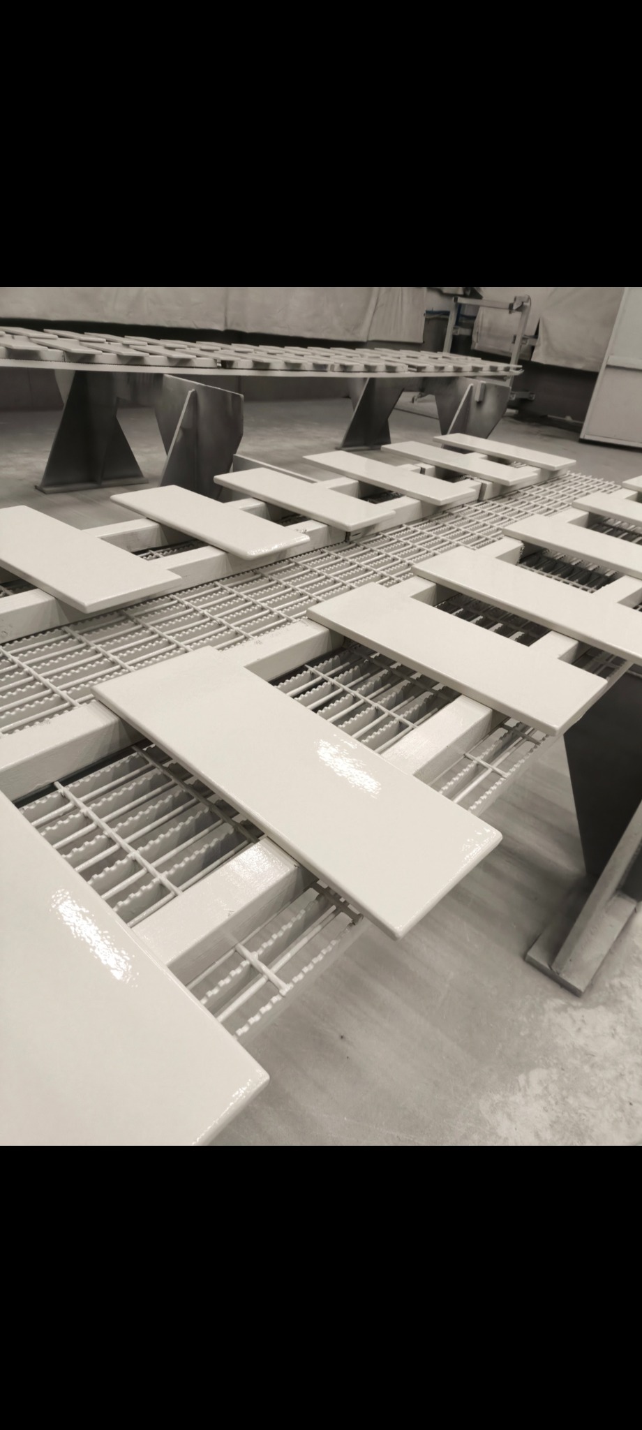 Białe, pomalowane elementy na metalowej kratownicy w hali produkcyjnej. Świeżo nałożona farba tworzy błyszczącą powierzchnię. Ujęcie z perspektywy.