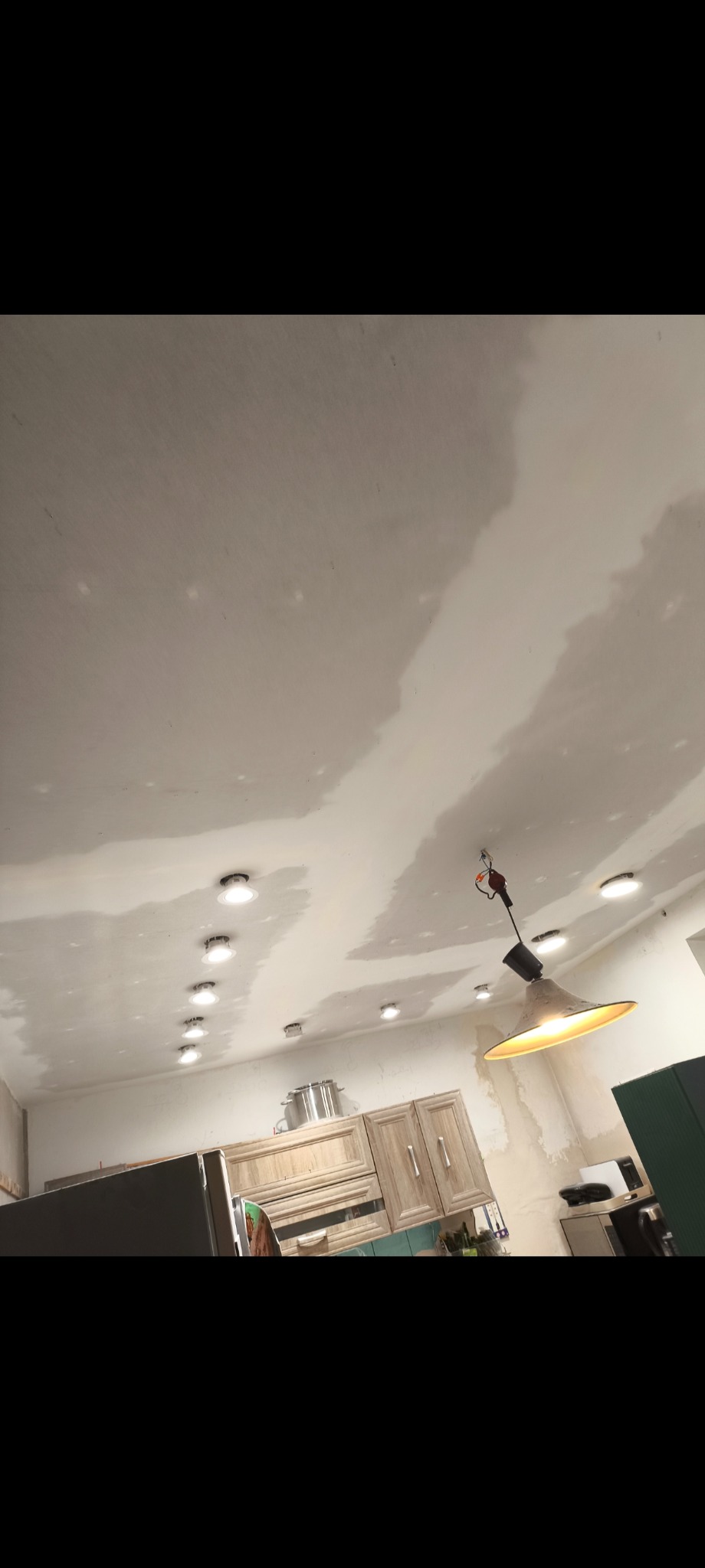 Nisko kątowe ujęcie sufitu w trakcie prac wykończeniowych, widoczne gładzie i zamontowane oświetlenie punktowe. W tle zabudowa kuchenna.