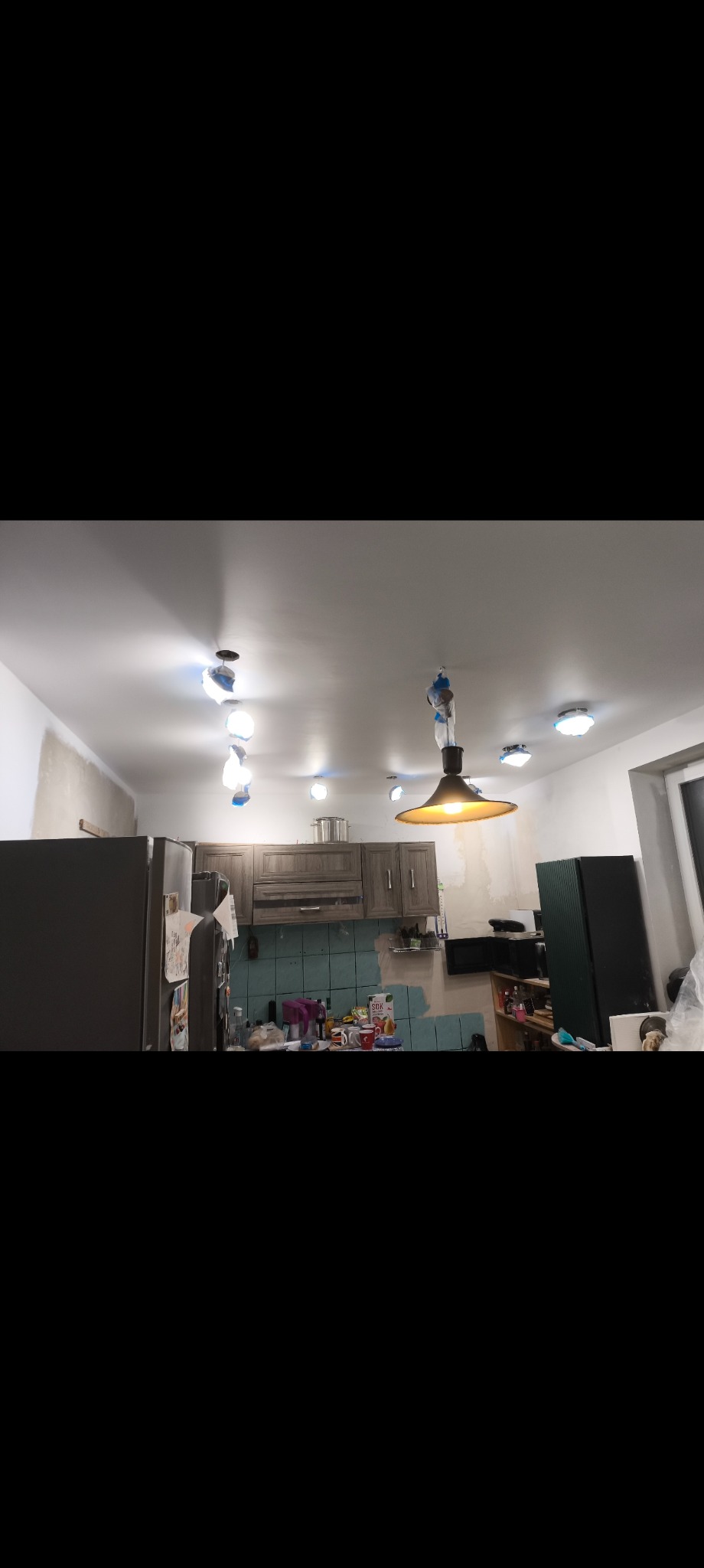 Kuchnia w trakcie remontu: widoczne przygotowane ściany, zabezpieczone lampy i częściowo położone płytki. Ujęcie z dołu, podkreślające etap prac wykończeniowych.