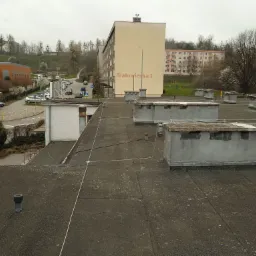 Widok z dachu budynku na osiedle mieszkaniowe, widoczne przewody instalacji odgromowej rozpięte na dachu.