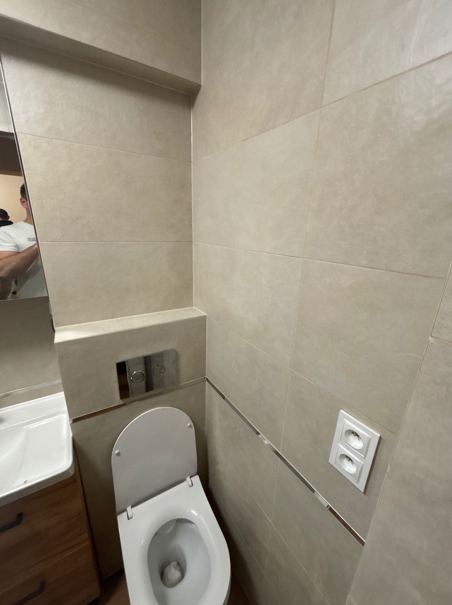 Beżowa łazienka po remoncie: płytki ścienne z dekoracyjną listwą, podwieszana toaleta z chromowanym przyciskiem, umywalka z szafką z drewnopodobnego materiału i lustro.