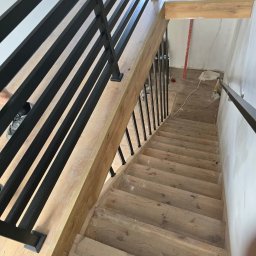 Dariusz Ernest PRECYZJA SPAWANIA - Schody drewniane z metalową balustradą w nowoczesnym stylu, widok z góry, jasne drewno, czarne elementy metalowe.