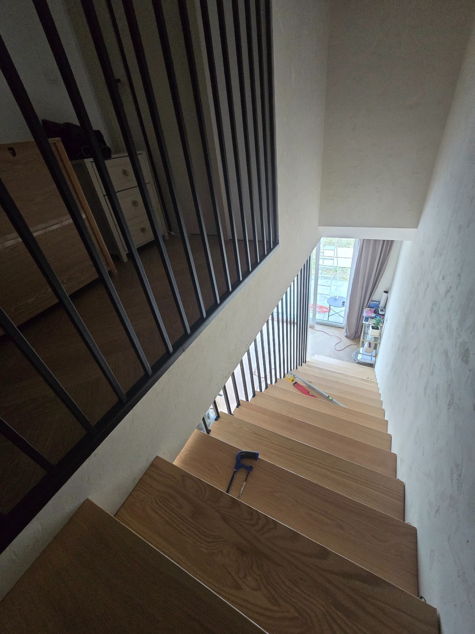 Montaż drewnianych schodów z metalową, minimalistyczną barierką. Widoczne narzędzia i naturalne światło wpadające przez okno na końcu biegu.