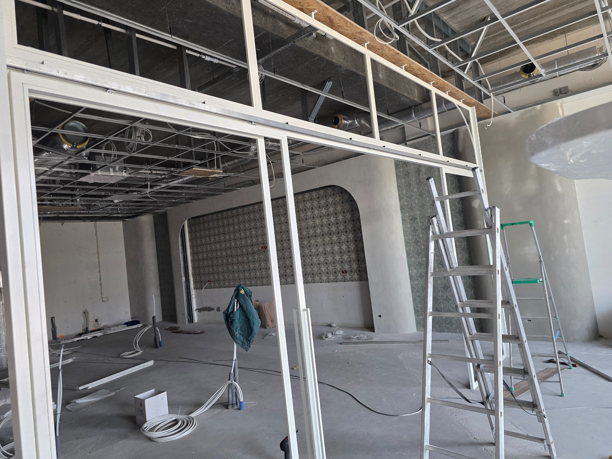 Montaż stalowej konstrukcji ścian działowych w surowym wnętrzu. Widoczne profile, drabiny i instalacje pod sufitem. Etap prac wykończeniowych.