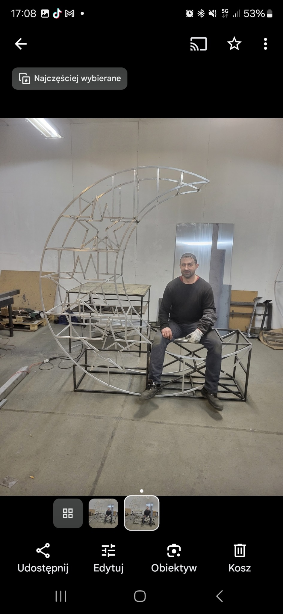 Spawacz siedzi na konstrukcji metalowej w kształcie księżyca i gwiazd. Widoczne spawy i elementy warsztatu, co podkreśla rzemieślniczy charakter usługi.