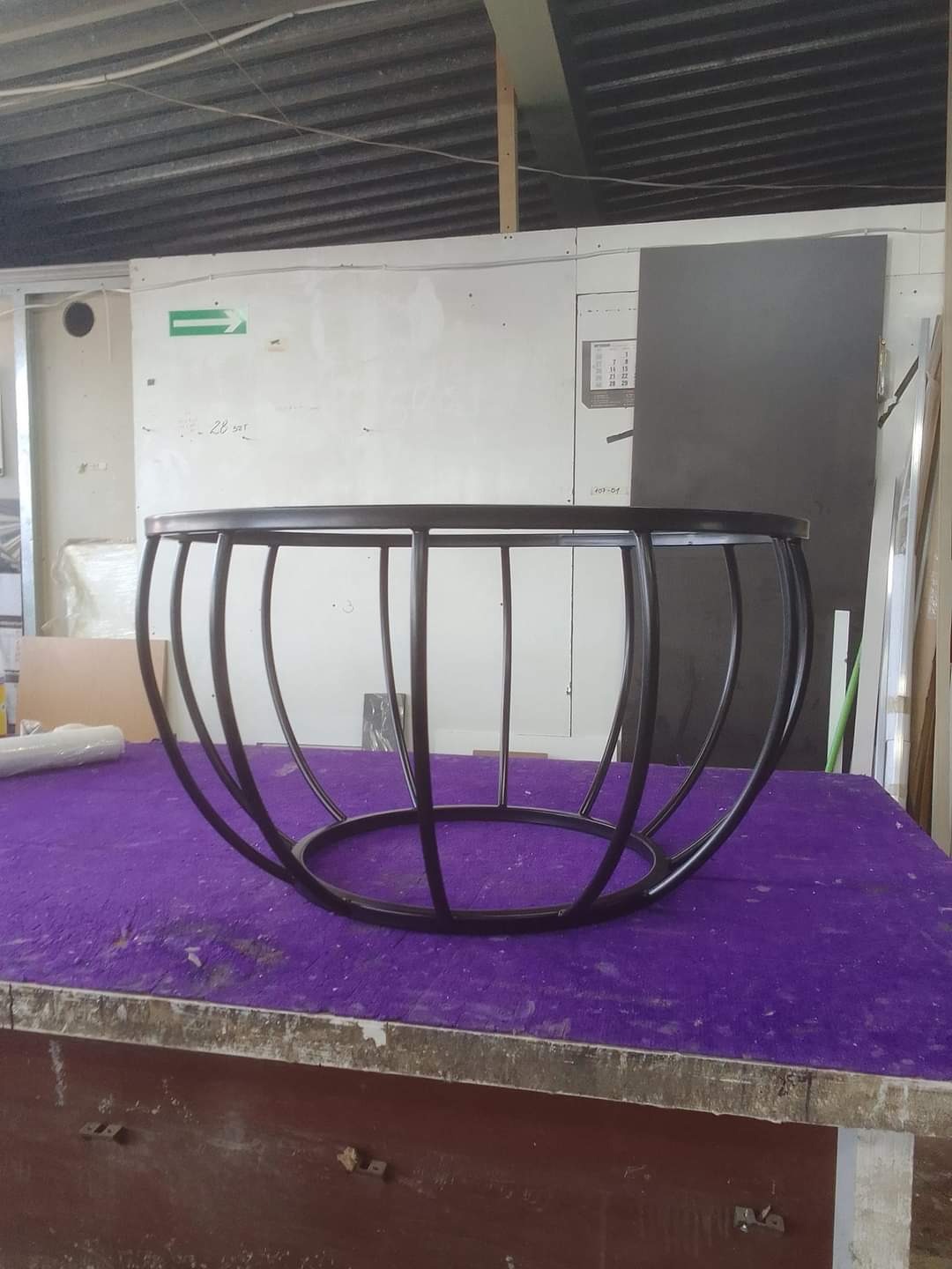 Okrągły stolik kawowy z metalową konstrukcją w stylu industrialnym, umieszczony na fioletowym blacie w warsztacie. Widoczne spawane elementy.