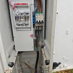 Pro Light Instalacje Elektryczne Łukasz Czajka - Otwarta skrzynka elektryczna z zaplombowanym rozłącznikiem bezpiecznikowym APATOR RBK00 i wyłącznikiem Lovato MB 3P T32, widoczne okablowanie na zewnątrz.