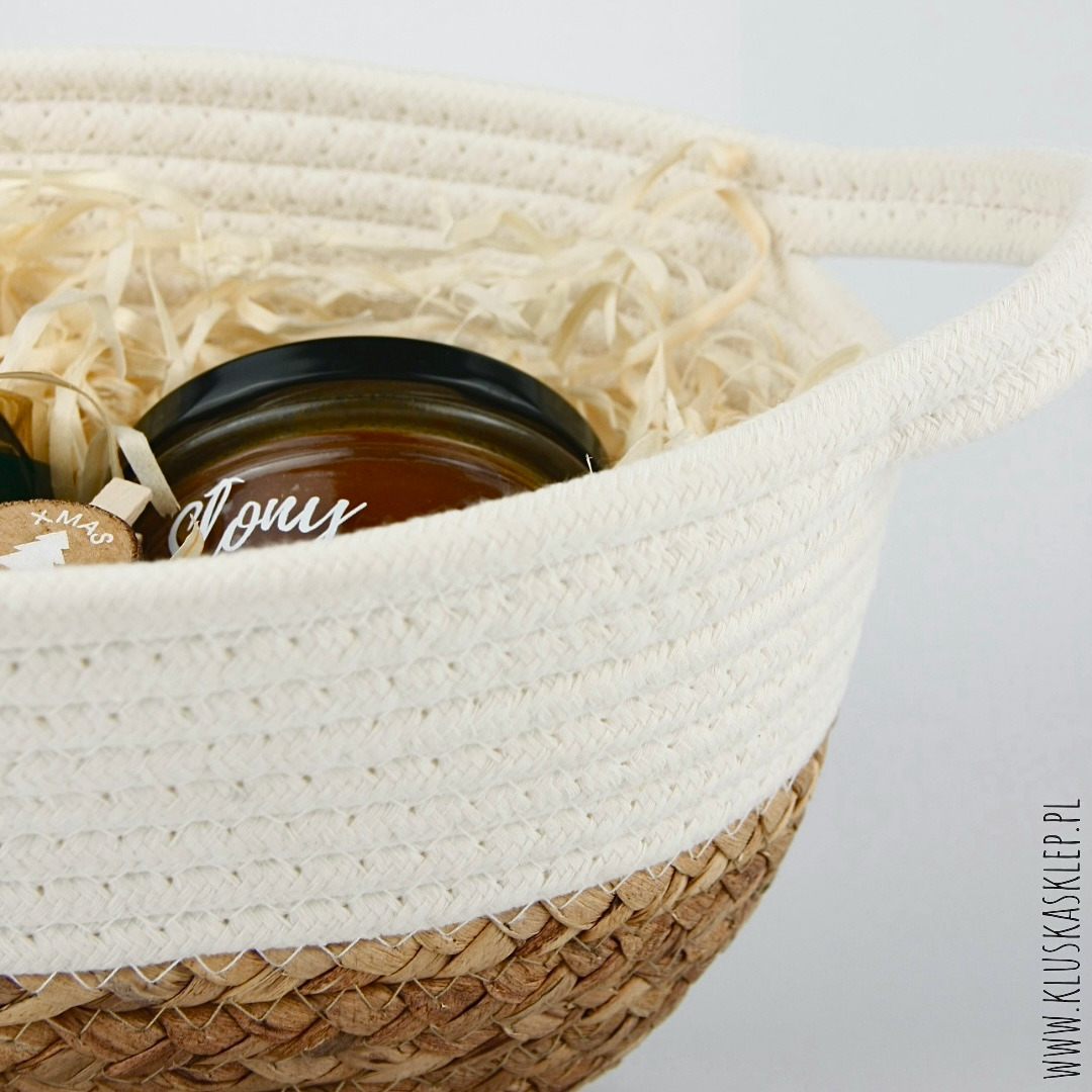 Ręcznie robiony kosz z jutową podstawą, wypełniony dekoracyjną wełną drzewną, zawierający słoik miodu z napisem 'Mony' i drewnianą zawieszką z motywem choinki.
