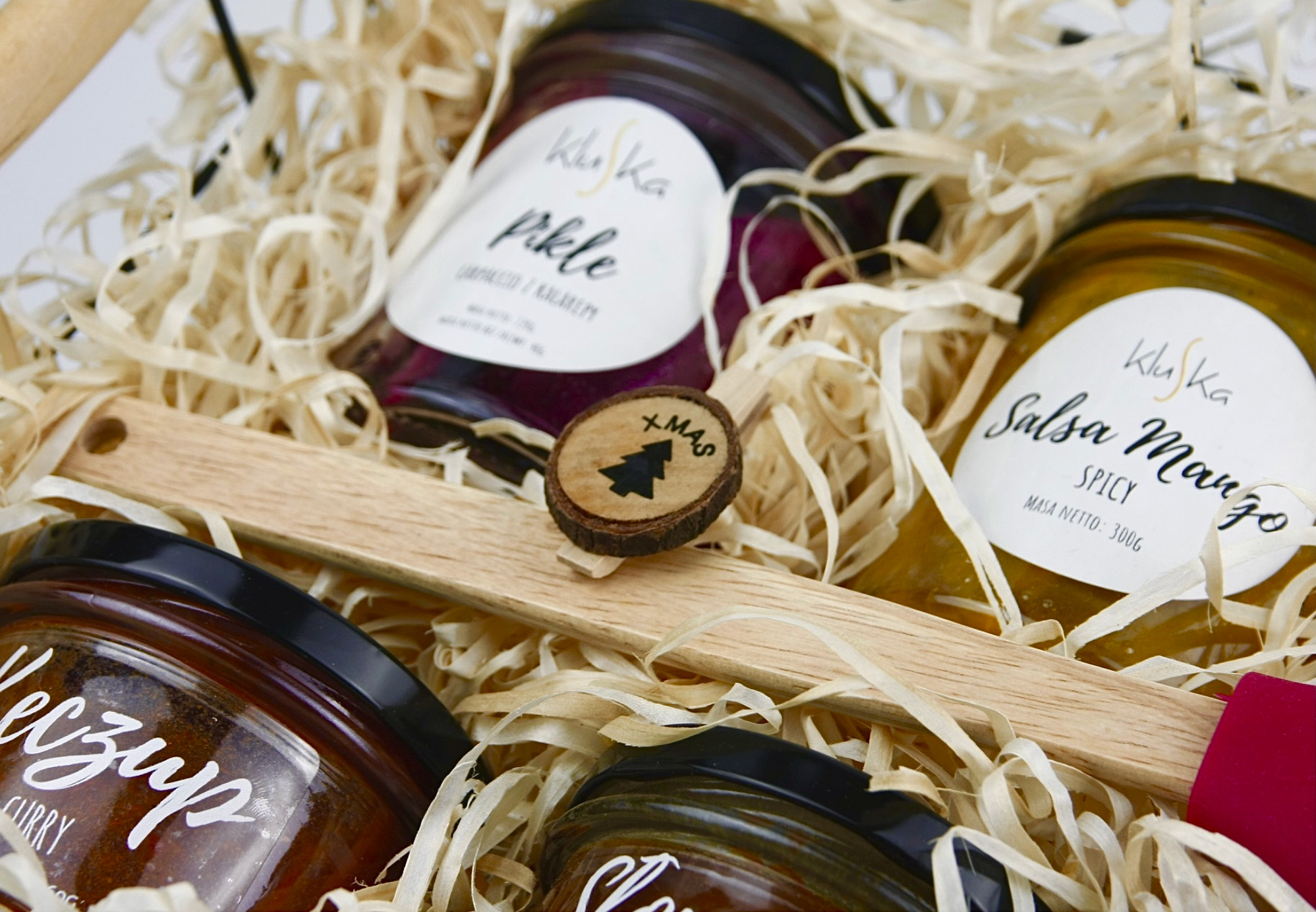 Kosz z lokalnymi przetworami marki Kluska z Gdyni: pikle z buraka, salsa mango spicy i ketchup curry, udekorowany drewnianym elementem z choinką, idealny na świąteczny prezent.