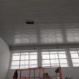 Montaż sufitu z paneli w dużej hali, widoczny podnośnik i zabezpieczone okna folią malarską.