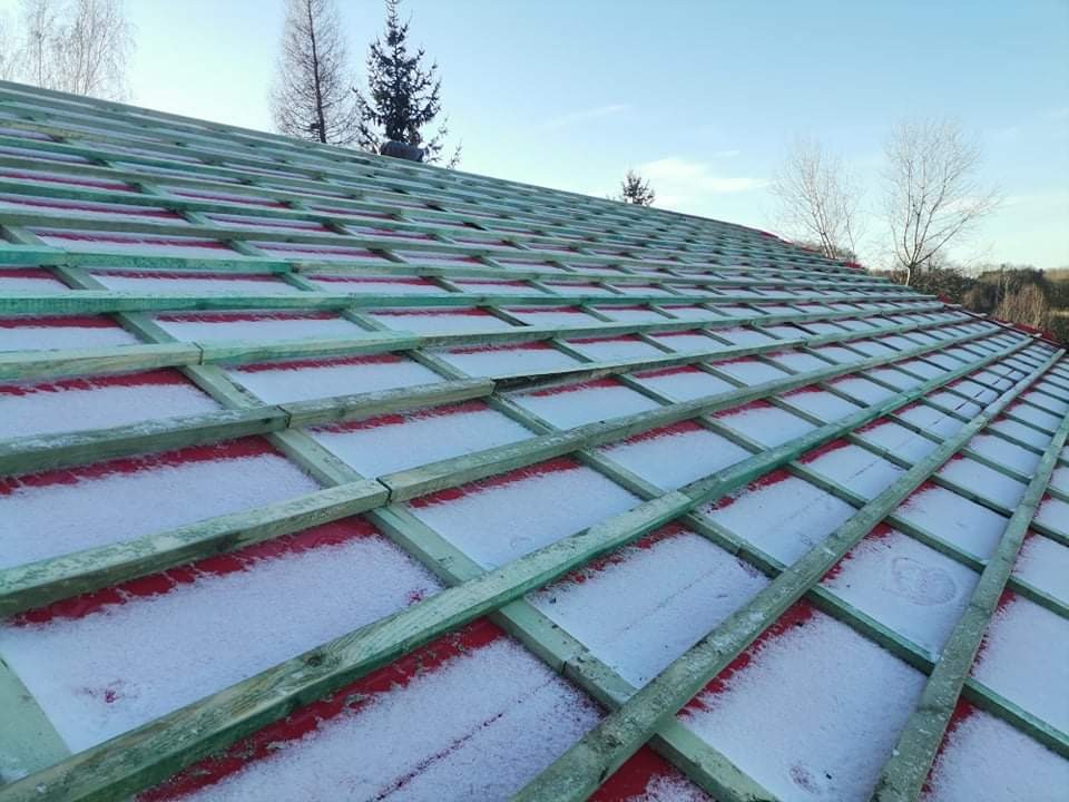 Konstrukcja dachu z zielonymi łatami i czerwoną membraną pokryta lekkim śniegiem, widok z dołu pod kątem.