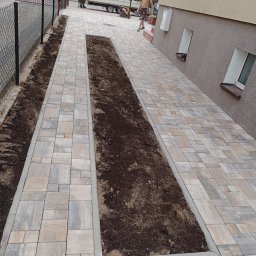 Solis - Roboty Ziemne Instalacje Sanitarne - Ścieżka z kostki brukowej w odcieniach szarości i beżu, z wydzielonymi pasami ziemi po bokach i na środku. Prace brukarskie w toku, widoczni pracownicy w tle.