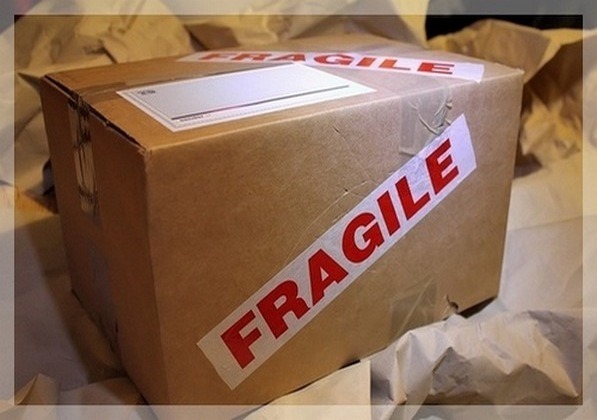 Kartonowe pudełko zaklejone taśmą z napisem 'FRAGILE' leżące na zmiętym papierze pakowym.