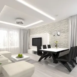 Jasne wnętrze salonu z białymi ścianami, panelami podłogowymi, nowoczesnym oświetleniem sufitowym i czarnymi krzesłami przy białym stole, z dekoracyjną ścianą z kamienia i telewizorem.