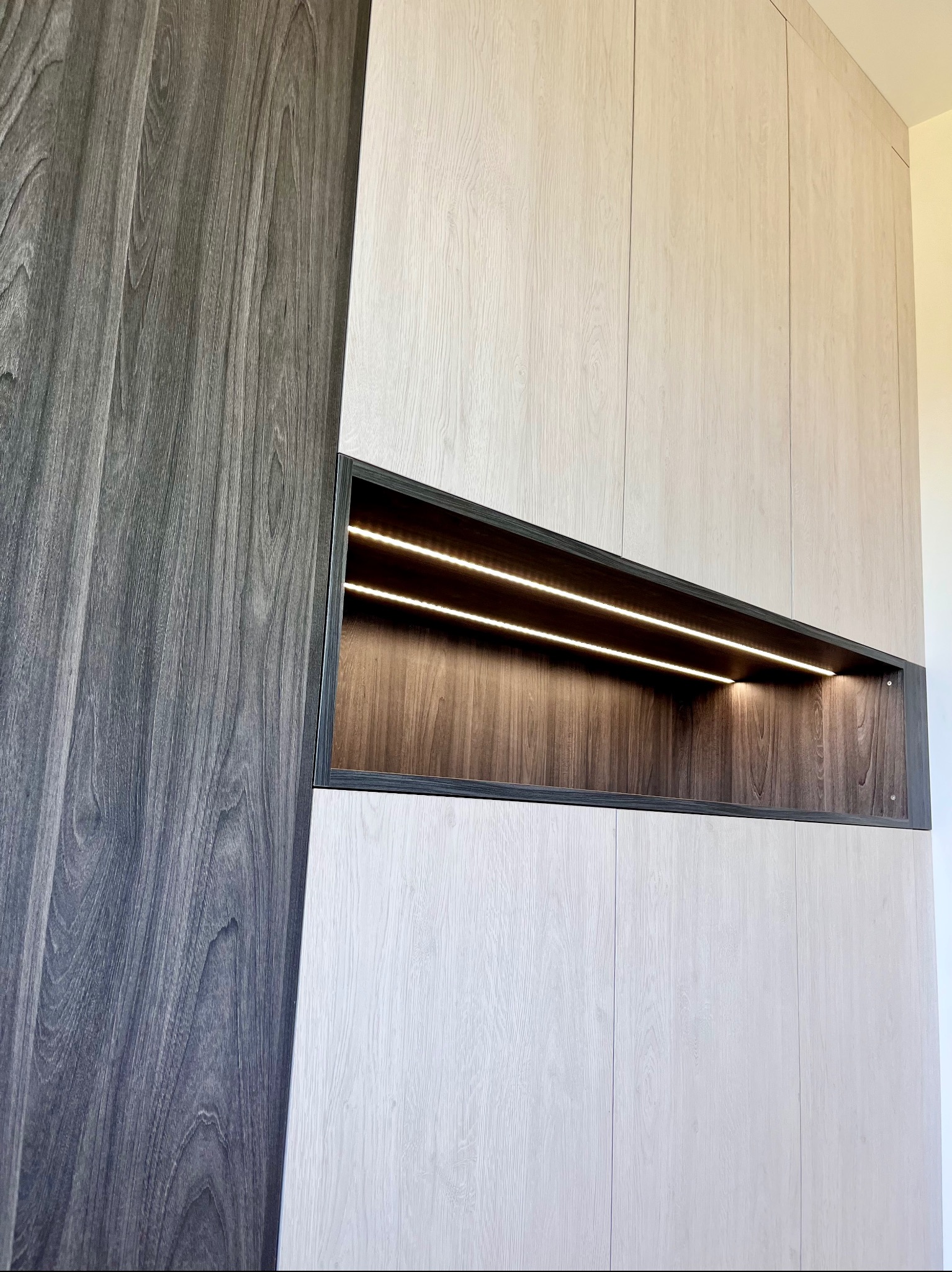 Nowoczesna szafa na wymiar z oświetleniem LED wnęki. Kontrastowe drewno: jasne fronty i ciemny bok. Minimalistyczny design, eleganckie wykończenie.