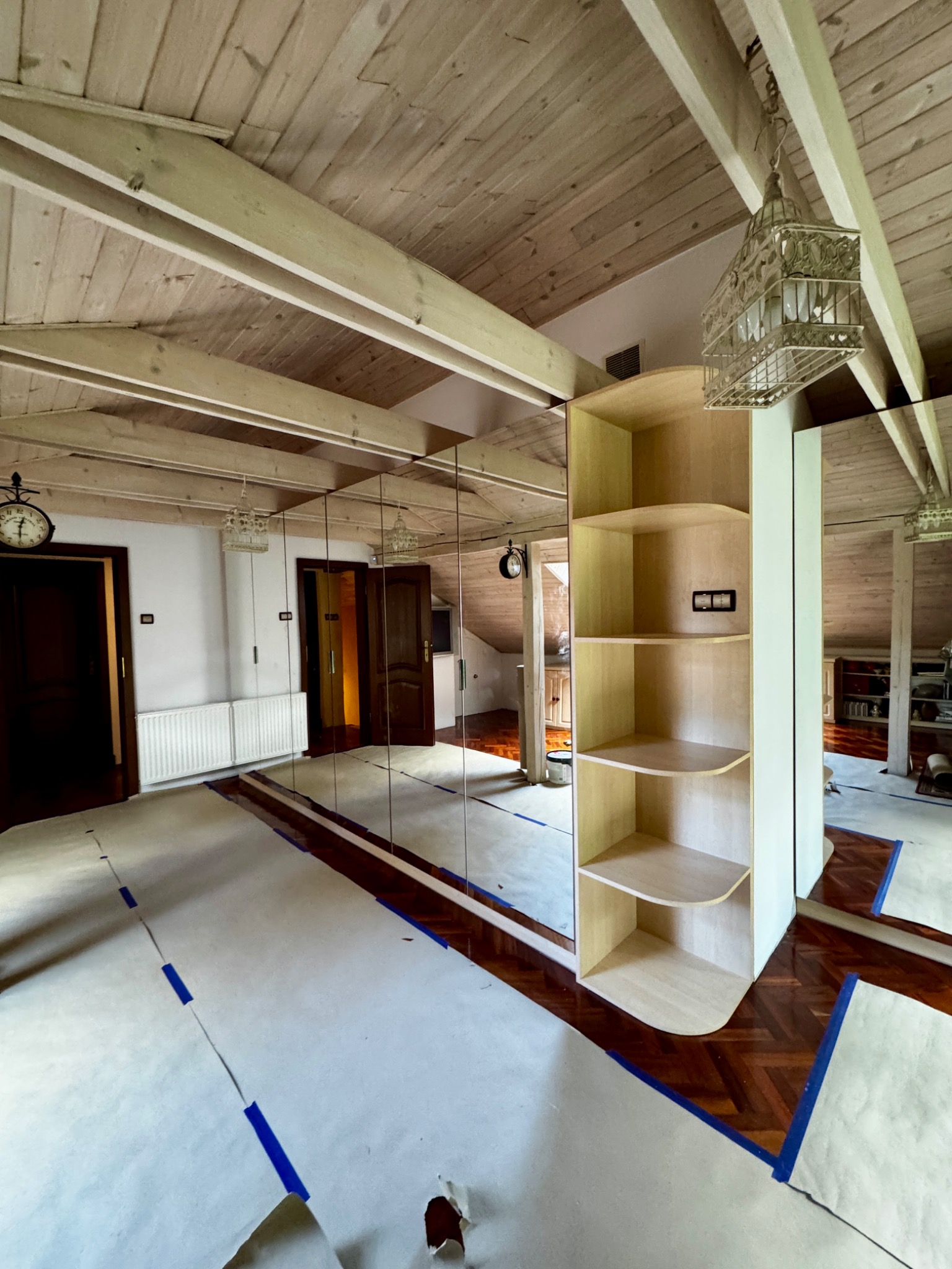 Montaż lustrzanej szafy wnękowej z półkami w pokoju na poddaszu z drewnianą boazerią. Podłoga zabezpieczona papierem malarskim.