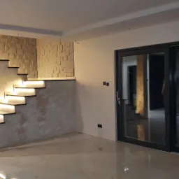 Nowoczesne wnętrze z podświetlanymi schodami, dekoracyjną ścianą z tr&oacute;jwymiarowych paneli i dużymi przesuwnymi drzwiami balkonowymi, ściany wykończone w odcieniach szarości i bieli, podłoga...