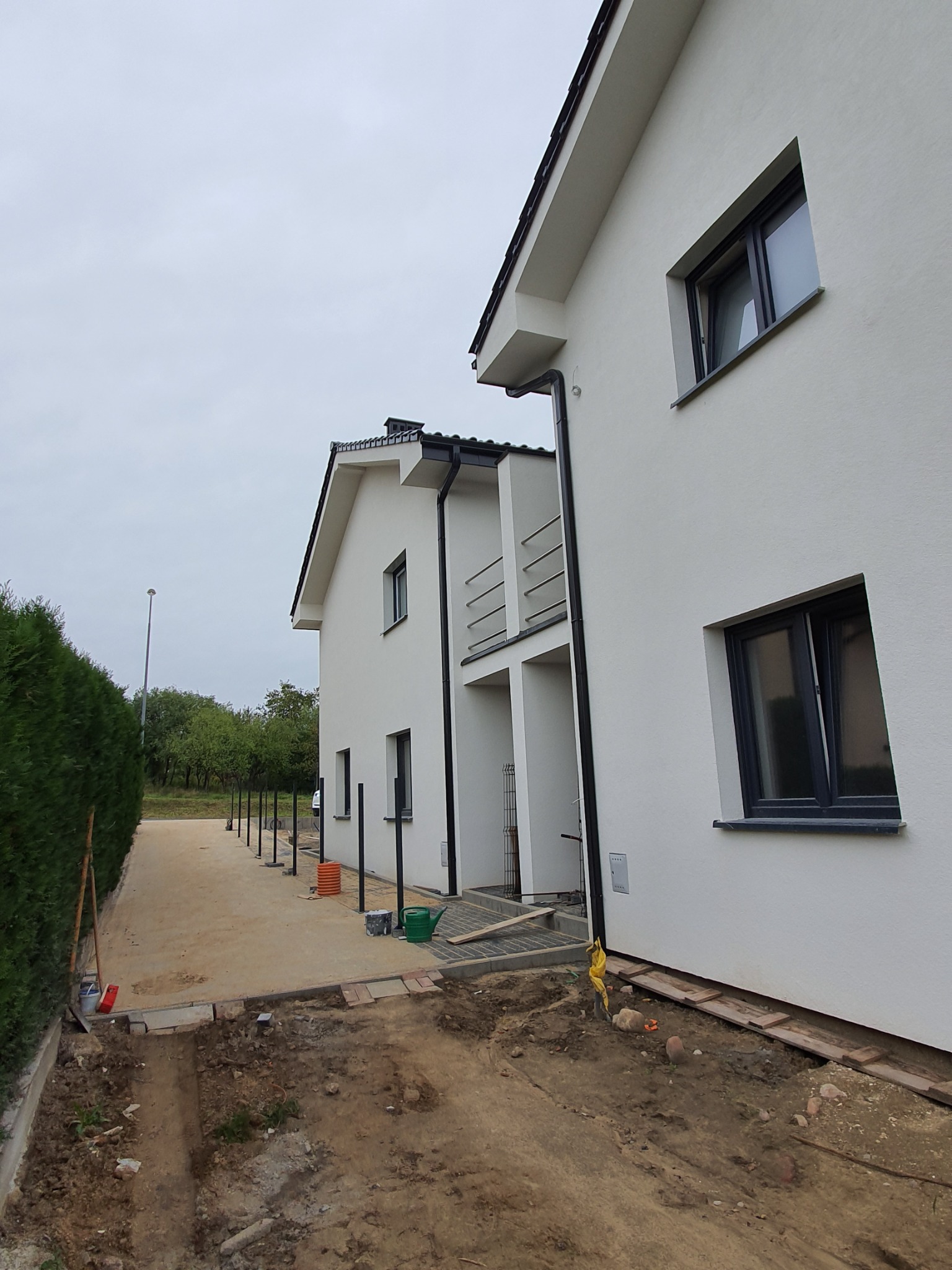 Nowoczesny dom murowany z białymi ścianami i czarną stolarką okienną, widok z boku na podwórze w trakcie prac wykończeniowych, widoczne przygotowania pod chodnik.