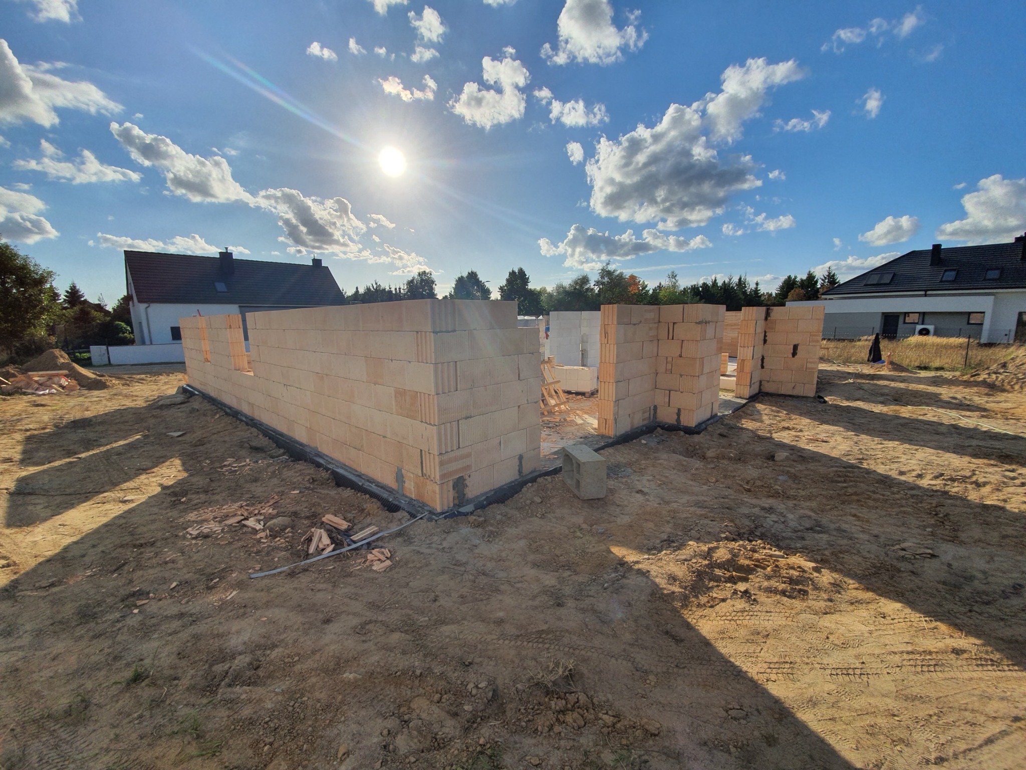 Wznoszenie ścian parterowego domu z bloczków na fundamencie, widok na plac budowy w słoneczny dzień.